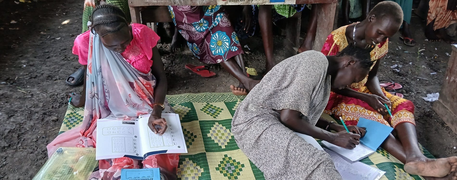 Kolme ihmistä istuu lattialla ja opiskelee Etelä-Sudanissa.